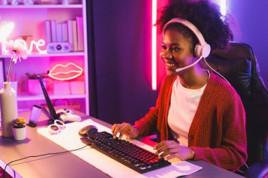 Oyun flama, Afrikalı kız Esport yetenekli takımıyla online kavga ediyor. Neon renkli aydınlatma odasında kulaklık takıyor. Rakiplerini kazanmak için strateji planlayan diğer oyuncularla konuşmak. Tatlandırıcı.