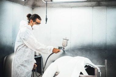 Koruyucu ekipmanlı otomotiv işçisi araba kaportasına sprey tabanca ya da oda atölyesindeki solunum boyasıyla renk boyası uyguluyor. Tamir için araba boyama servisi. Oxus.