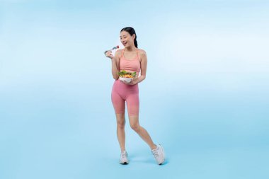 Spor giyim mağazasında elinde meyve ve sebze dolu salata kasesi tutan genç bir Asyalı kadın. Doğal gençlik ve uygun vücut yaşam tarzı izole edilmiş arka planda dengeli beslenme. Kuvvetli