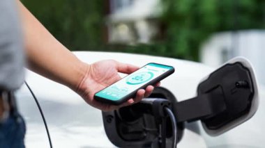 Akıllı telefon ekranı akıllı EV mobil uygulama üzerinde pil durumu EV araba garajdaki ev şarj istasyonu ile elektrik şarj ederken. Geleceğin yenilikçi EV arabası ve enerji sürdürülebilirliği. İnceleyin