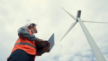 Gökyüzü arka planına sahip bir rüzgar türbini üzerinde çalışan mühendis. Yenilenebilir ve sürdürülebilir enerjinin gelecekteki üretimi için yenilikçi bir ideal. Rüzgar türbininden enerji üretimi.