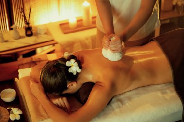 Sıcak bitkisel top spa masaj vücut tedavisi, masör kadın vücuduna nazikçe şifalı bitki torbası bastırıyor. Aromaterapi tesisinin sakinliği ve dinginliği kaplıca salonundaki mumların sıcacık ışığında. Sessiz.