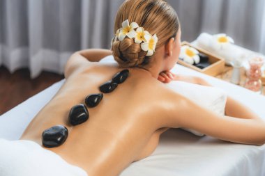 Lüks tatil köyündeki kaplıcalarda sıcak taş masajı. Gün ışığı sükunet ortamında, mutlu kadın müşteri bazalt taş masajından zevk alıyor. Rahatlatıcı bir sıcaklıkla vücudun üzerinde süzülüyor. Sessiz.