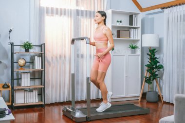 Enerjik ve güçlü atletik Asyalı kadın evde koşu makinası çalıştırıyor. Formda fiziğin takibi ve ev çalışması ve eğitimle sağlıklı yaşam tarzına bağlılık. Kuvvetli