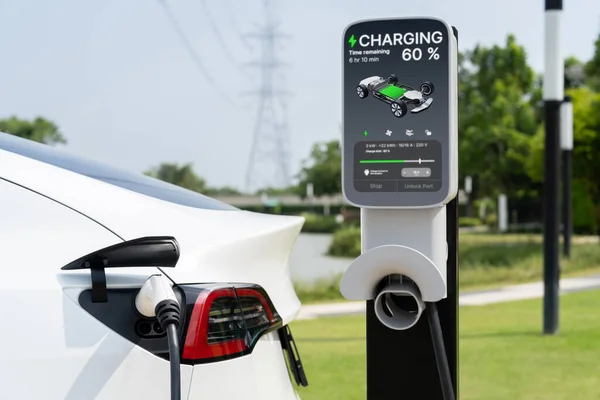 Electric vehicle or EV car recharge battery at charging station connected to power grid tower electrical industrial facility as electrical industry for eco friendly vehicle utilization. Expedient