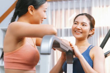 Enerjik ve güçlü atletik Asyalı kadın evde spor arkadaşı ya da antrenörü ile birlikte eliptik koşu makinesiyle koşuyor. Formda fiziğin takibi ve sağlıklı yaşam tarzına bağlılık. Kuvvetli