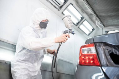 Tam korumalı ekipmanlı otomotiv işçisi sprey tabanca ya da oda atölyesindeki solunum cihazı boyasıyla araba kaportasına ustalıkla renk boyası uygular. Tamir için araba boyama servisi. Oxus.