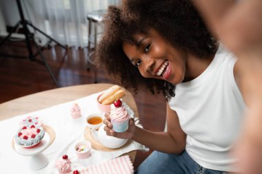 Genç ve güzel Afrikalı blogcu akıllı telefondaki selfie ile konsept özel mutfak konseptinde kek sunuyor. Favori tatlı fırın yemeğiyle sosyal medyanın yaratılması. Tatlandırıcı.
