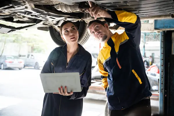 Dwóch Mechaników Pracujących Razem Pod Podnoszonym Samochodem Przeprowadza Inspekcję Samochodu — Zdjęcie stockowe