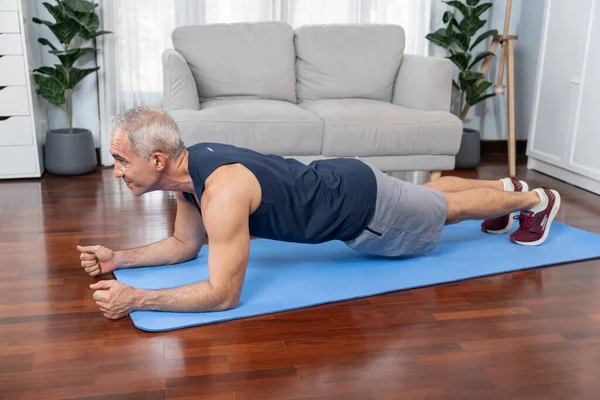 Athletic and sporty senior man planking on fitness exercising mat at home exercise as concept of healthy fit body lifestyle after retirement. Clout