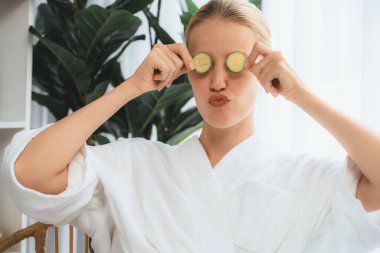 Elinde taze salatalık dilimleri tutan ve bornoz giyen bir kadın tatil köyünde ya da otelde lüks yüz derisi kaplıcalarının tadını çıkarıyor. Yüz ve güzellik tedavisi için cilt bakımı. Sessiz.