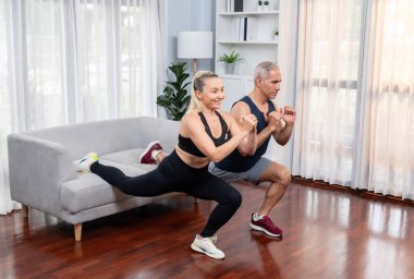 Aktif ve formda yaşlı çiftler oturma odasında egzersiz yapmadan önce mobilya kullanarak ısınma ve esneme hareketleri yapıyorlar. Emeklilikten sonra sağlıklı yaşam tarzı konsepti. Etki