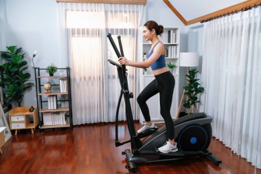 Enerjik ve güçlü atletik Asyalı kadın evde eliptik koşu makinesiyle koşuyor. Formda fiziğin takibi ve ev çalışması ve eğitimle sağlıklı yaşam tarzına bağlılık. Kuvvetli