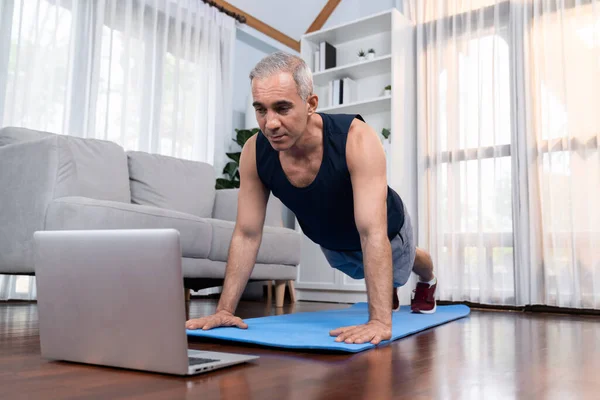 Athletic and sporty senior man doing pushup on exercising mat while watching instruction from online video at home exercise as concept of healthy fit body lifestyle after retirement. Clout