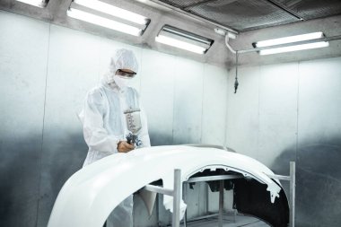 Tam korumalı ekipmanlı otomotiv işçisi sprey tabanca ya da oda atölyesindeki solunum cihazı boyasıyla araba kaportasına ustalıkla renk boyası uygular. Tamir için araba boyama servisi. Oxus.