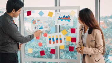 İş adamları ofisteki proje planlama kurulunda çalışıyor ve proje gelişimini analiz etmek için iş arkadaşlarıyla sohbet ediyorlar. Düzenli olması için cama yapıştırılmış yapışkan notlar kullanıyorlar. Jivy