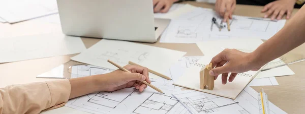 Professional architect hand draws a blueprint on table with architectural document and wooden block scatter around at office. Design and Planing concept. Focus on hand. Closeup. Delineation.