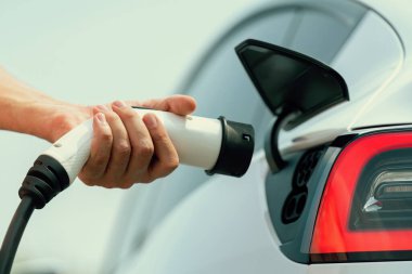 Dışarıdaki şarj istasyonundan EV şarj aletini şarj etmek için elektrikli araca elle tak. Alternatif temiz ve sürdürülebilir enerji kavramına sahip taze gün ışığı ortamı. Kalıcı
