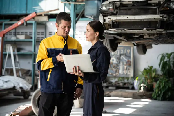 Two vehicle mechanic working together, conduct car inspection with laptop. Automotive service technician in uniform carefully make diagnostic troubleshooting to identify error. oxus