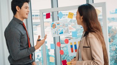 İş adamları ofisteki proje planlama kurulunda çalışıyor ve proje gelişimini analiz etmek için iş arkadaşlarıyla sohbet ediyorlar. Düzenli olması için cama yapıştırılmış yapışkan notlar kullanıyorlar. Jivy