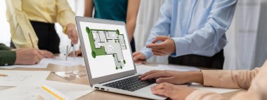 Profesyonel mimar, mimari dökümanlar etrafa saçılmışken toplantı masasındaki planların değiştirilmesiyle ilgili tartışmalarda çevre dostu evin planına karar veriyor. - Yakın çekim. Tanımlama