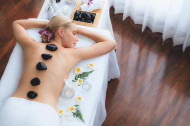 Lüks tatil beldesindeki kaplıca salonunda sıcak taş masajı. Gündüz huzurlu ortam, mutlu kadın müşteri bazalt taşı masajının keyfini çıkarıyor. Sessiz.