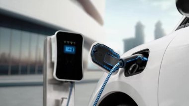 Modern ve fütüristik bina arka planında akıllı EV şarj istasyonundan elektrikli araba şarj oluyor. Alternatif ve sürdürülebilir enerji kullanan şarj edilebilir EV arabaların teknolojik gelişimi. İnceleyin