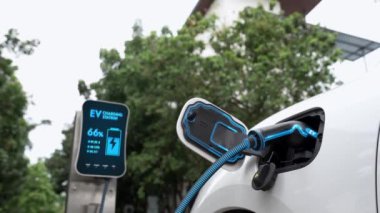 Doğal yeşil araba parkındaki ekolojik temiz enerji şarj istasyonundan gelen fütürist akıllı EV şarj aletinin şarj ettiği elektrikli araba. Alternatif enerji kullanan gelecekçi çevre dostu elektrikli araba. İnceleyin