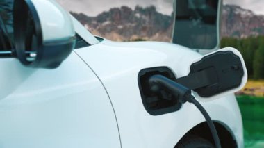 Elektro jeneratör sürücüsüyle enerji sürdürülebilir araba gücü, şarj istasyonunda şarj edilen batarya, ilerici seyahat konsepti için dağ zeminine sahip. Temiz ortamın sembolü olarak doğadaki EV otomobil.
