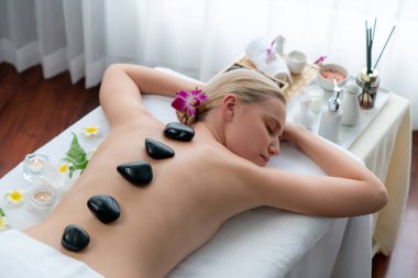 Lüks tatil köyündeki kaplıcalarda sıcak taş masajı. Gün ışığı sükunet ortamında, mutlu kadın müşteri bazalt taş masajından zevk alıyor. Rahatlatıcı bir sıcaklıkla vücudun üzerinde süzülüyor. Sessiz.