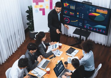 Modern toplantı odasındaki TV ekranında veri analizi paneliyle üst görünüm iş sunumu. İş adamlarının iş pazarlama stratejisini planlamak için beyin fırtınası yapması ya da birlikte çalışması. Uyum