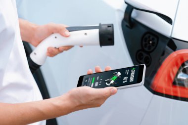 EV 'yi şarj etmek için elektrikli araca EV şarj prizi tak, akıllı telefon EV uygulamasında pil durumu görüntüsü. Ulaşım için alternatif temiz ve sürdürülebilir enerji. Kalıcı