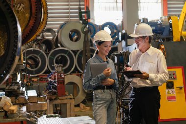 Metal imalatında makine mühendisliği denetleyicisi olarak liderlik örneğini sunan çelik endüstriyel makineyi incelemek için dizüstü bilgisayar kullanan fabrika mühendisi ve asistan..