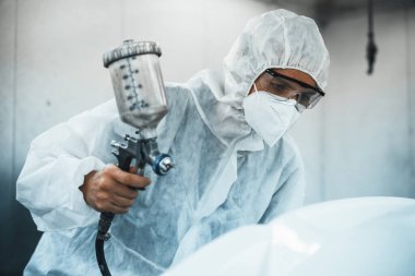 Tam korumalı ekipmanlı otomotiv işçisi sprey tabanca ya da oda atölyesindeki solunum cihazı boyasıyla araba kaportasına ustalıkla renk boyası uygular. Tamir için araba boyama servisi. Oxus.