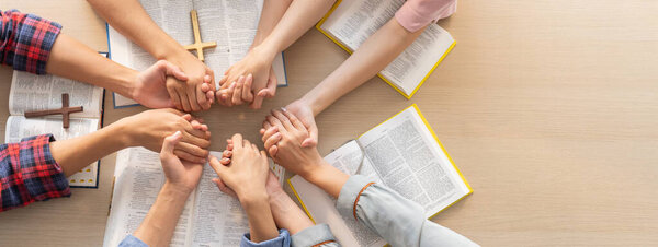 Cropped image of group of people praying together while holding hand on holy bible book at wooden church. Concept of hope, religion, faith, christianity and god blessing. Top view. Burgeoning.