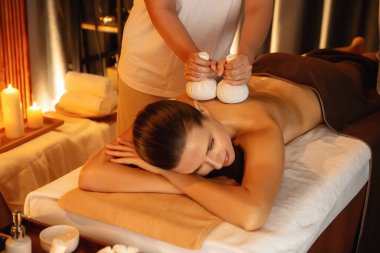 Sıcak bitkisel top spa masaj vücut tedavisi, masör kadın vücuduna nazikçe şifalı bitki torbası bastırıyor. Aromaterapi tesisinin sakinliği ve dinginliği kaplıca salonundaki mumların sıcacık ışığında. Sessiz.
