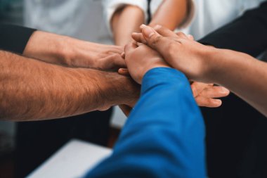 Çeşitli ofis çalışanlarından oluşan bir grup, ofis odasında el ele vererek iş sinerjisini ve iş yerindeki güçlü verimli takım çalışmasını sembolize ediyor. İş çalışanları arasındaki işbirliği ve birlik. Tedbirli