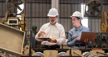 Metal imalatında makine mühendisliği denetleyicisi olarak liderlik örneğini sunan çelik endüstriyel makineyi incelemek için dizüstü bilgisayar kullanan fabrika mühendisi ve asistan..