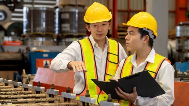 Ağır sanayi fabrikasındaki çelik üretim hattında endüstriyel malların optimal kalitede üretimi için mühendis tarafından denetlenirken fabrika işçisi metal damgalama makinesini çalıştırıyor. Örnek gösteriliyor