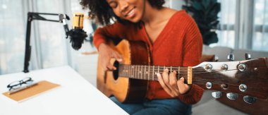 Genç Afrikalı Amerikalı müzisyenin sunucu kanalı gitar çalıyor, şarkı söylüyor, stüdyoda akıllı telefondan yayın yapıyor. Ekipman kulaklıkları dekorasyonu ve mikrofon kaydı. Tatlandırıcı.