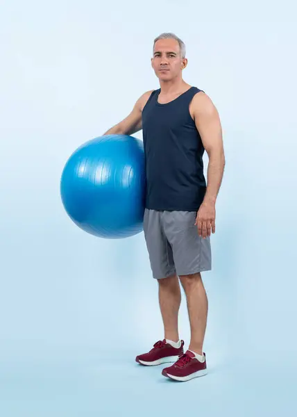 Full body length shot athletic and sporty senior man with fitness exercising ball in standing posture on isolated background. Healthy active and body care lifestyle after retirement. Clout