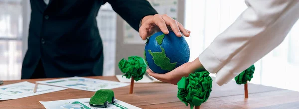 Business people holding paper earth together over office table. Green corporate company implementing eco-friendly policy to reduce CO2 emission and conserve green environment concept. Trailblazing
