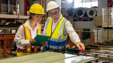 Fabrika mühendisi, metal levha ürünü üzerinde kalite kontrolü yapmak ve ağır endüstriyel çelik damgalama veya oluşturma makinesini denetlemek için iş arkadaşıyla işbirliği yapar. Örnek gösteriliyor