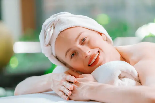 Closeup of beautiful women in white towel relaxes on spa bed while looking at camera. Young gorgeous female wearing white towel during waiting for body massage at spa. Side view. Tranquility