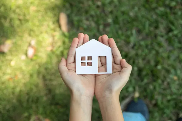 stock image Top view hand hold house icon, presenting house loan opportunity as part of real estate sales. Promoting eco-smart homes, embodying vision for sustainable bright future nurturing with nature. Gyre