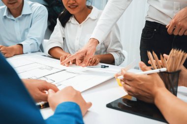 Mimari proje üzerinde birlikte çalışan çeşitli inşaat mühendisi ve müvekkil grupları, inşaat planını gözden geçirip toplantı masasında plan oluşturuyorlar. Tedbirli