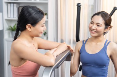 Enerjik ve güçlü atletik Asyalı kadın evde spor arkadaşı ya da antrenörü ile birlikte eliptik koşu makinesiyle koşuyor. Formda fiziğin takibi ve sağlıklı yaşam tarzına bağlılık. Kuvvetli