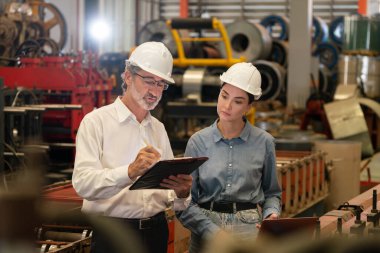 Metal imalatında makine mühendisliği denetleyicisi olarak liderlik örneğini sunan çelik endüstriyel makineyi incelemek için dizüstü bilgisayar kullanan fabrika mühendisi ve asistan..