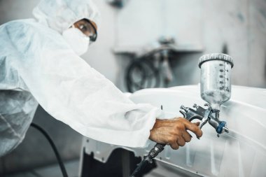Tam korumalı ekipmanlı otomotiv işçisi sprey tabanca ya da oda atölyesindeki solunum cihazı boyasıyla araba kaportasına ustalıkla renk boyası uygular. Tamir için araba boyama servisi. Oxus.