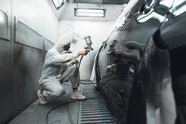 Tam korumalı ekipmanlı otomotiv işçisi sprey tabanca ya da oda atölyesindeki solunum cihazı boyasıyla araba kaportasına ustalıkla renk boyası uygular. Tamir için araba boyama servisi. Oxus.